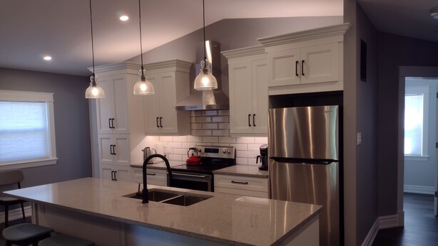 A modern kitchen with white cabinets, a stainless steel refrigerator, a large island with bar stools, and pendant lighting.