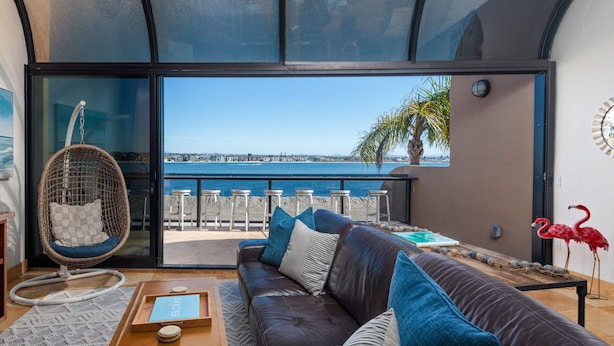 A modern living room with a leather sofa, a hanging chair, and a view of the sea.