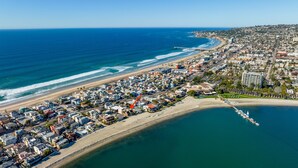 An aerial view of a coastal town with a beach, a pier, and a dense urban area with buildings.