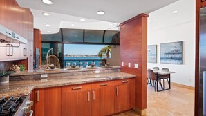 A modern kitchen with wooden cabinets, a granite countertop, and a view of the sea.