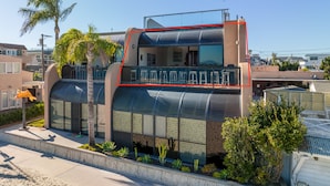 A modern house with a unique curved design, a balcony with stools, and a view of the surrounding neighborhood.