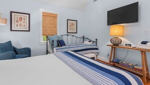 Un dormitorio con cama, escritorio, silla, televisor y obras de arte enmarcadas en las paredes.