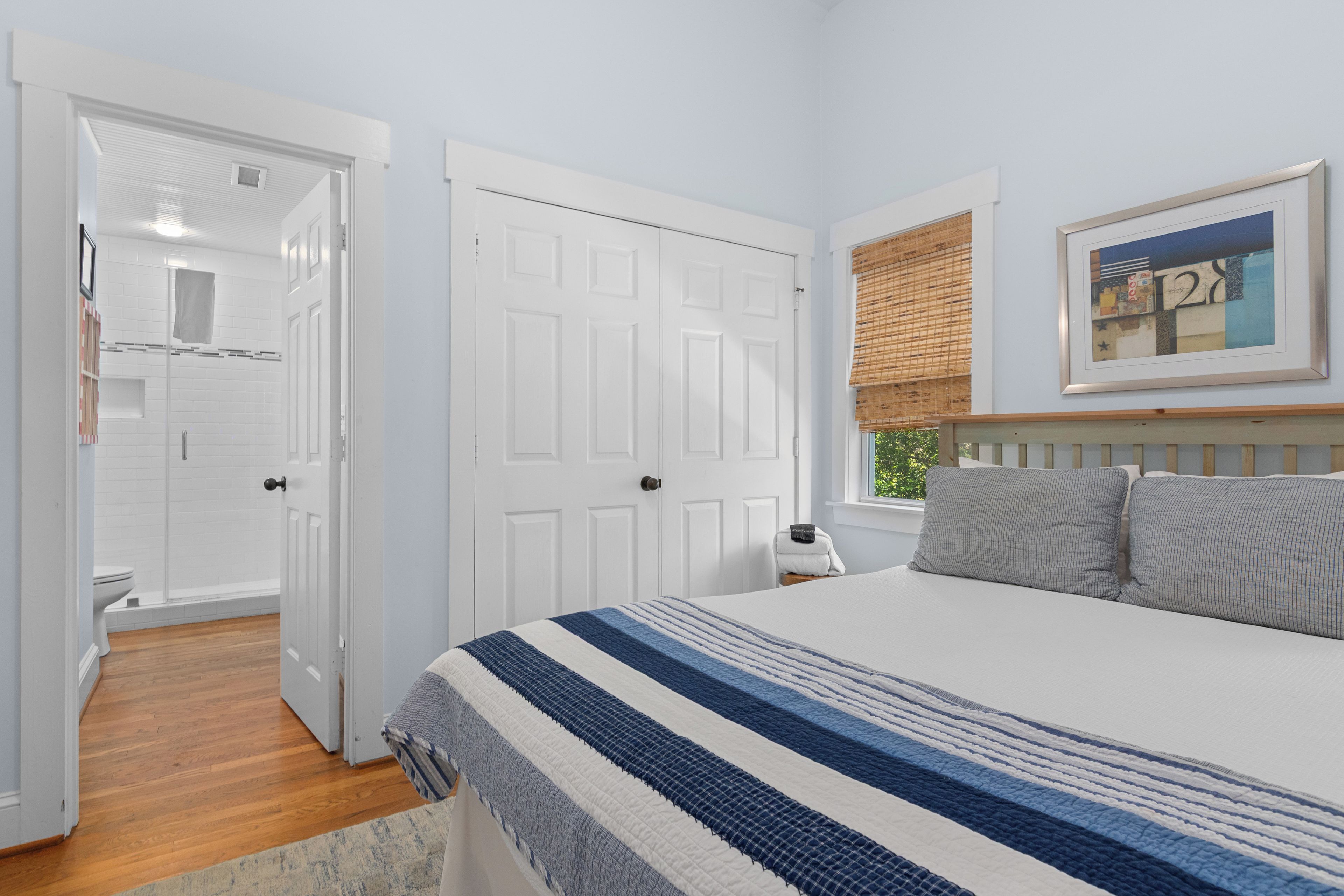 A bedroom with a bed, a nightstand, a window with blinds, and a door leading to a bathroom.
