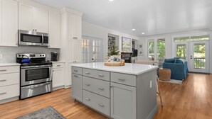Una cocina moderna con electrodomésticos de acero inoxidable, una isla grande con cajones y vistas a una sala de estar con un sofá azul.