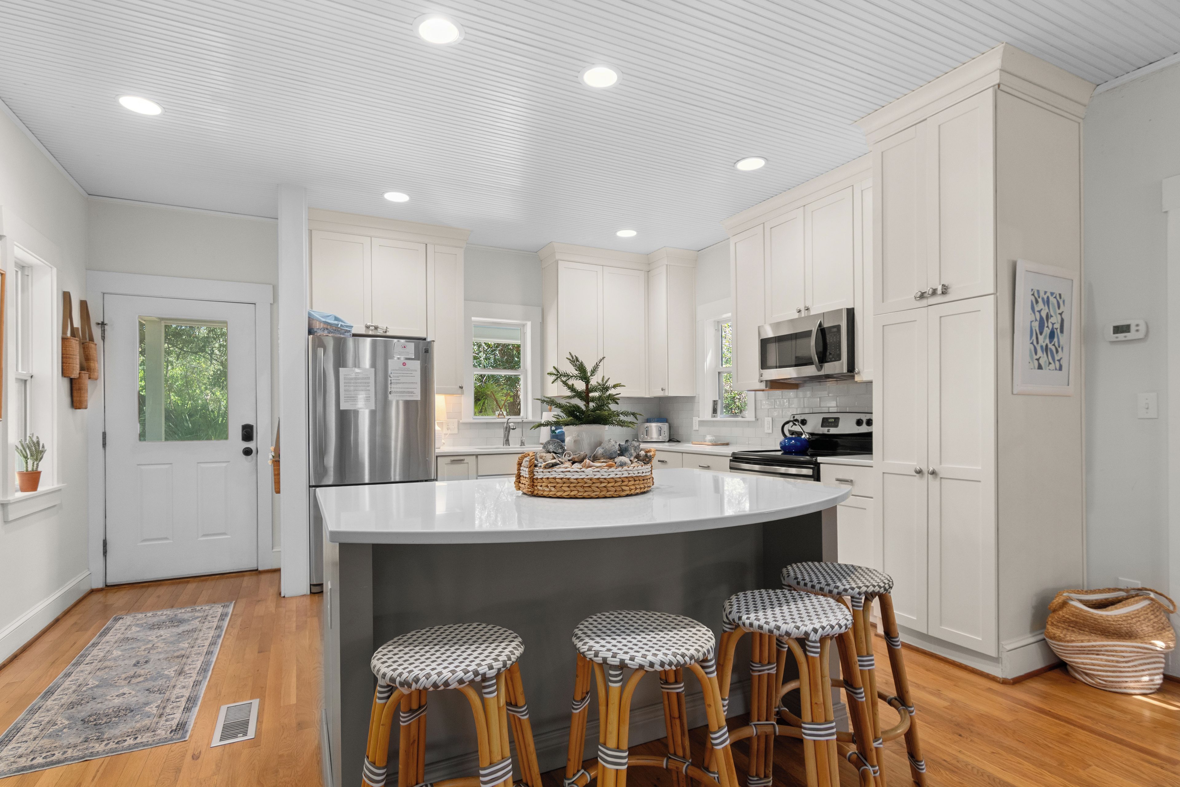 A modern kitchen with white cabinetry, stainless steel appliances, and a central island with bar stools.