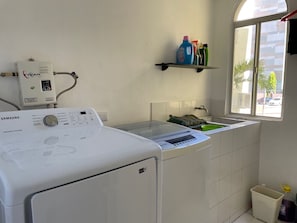 Un área de lavandería con lavadora y secadora Samsung, una ventana pequeña y un estante con productos de limpieza.