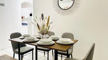 Un comedor con una mesa dispuesta para cuatro personas, sillas, un jarrón decorativo con plantas y un espejo colgado en la pared.