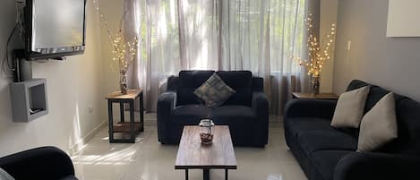 Ein Wohnzimmer mit einer dunklen Couch, einem Couchtisch und einem an der Wand befestigten Fernseher.