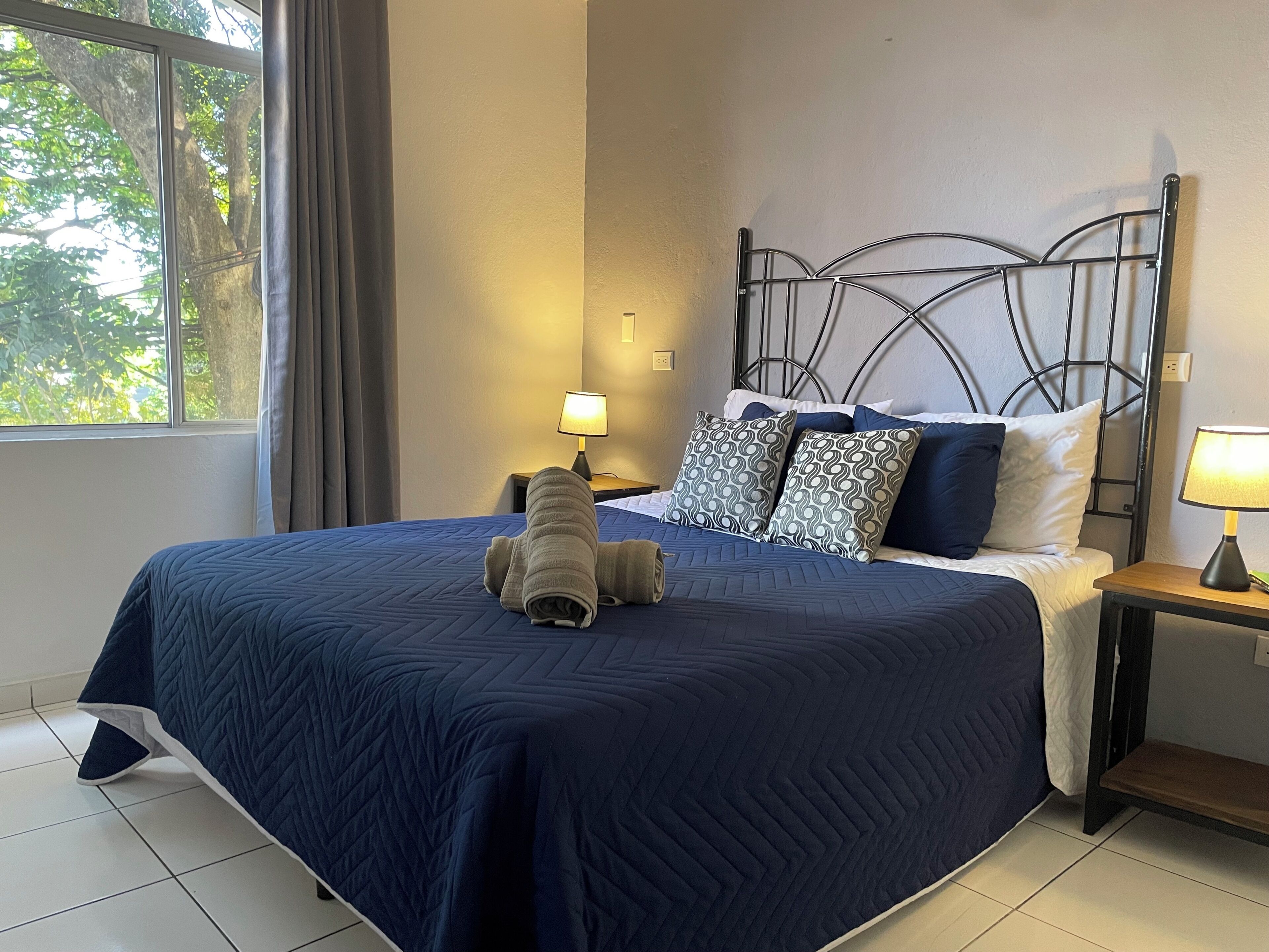 Un lit bien fait, avec une couette bleue, un oreiller à motifs et une lampe de chevet posée sur une table de nuit.