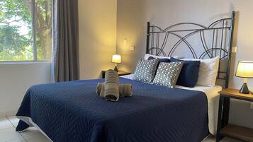 A neatly made bed with a blue quilt, a patterned pillow, and a bedside lamp on a nightstand.