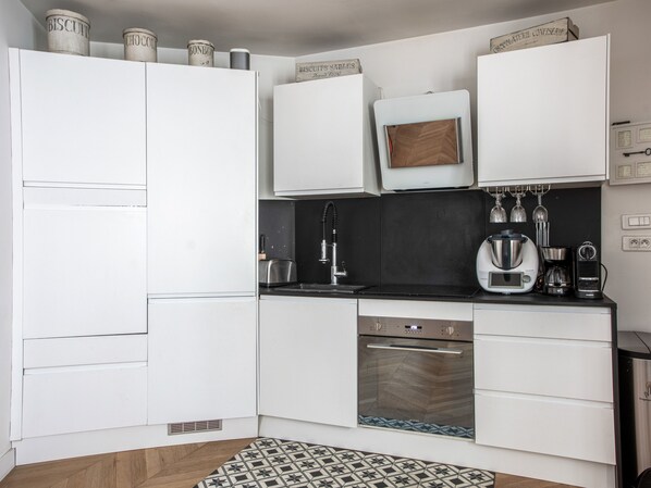 A modern kitchen with white cabinets, a black countertop, and a built-in oven. There are stainless steel appliances, including a coffee maker and a toaster.