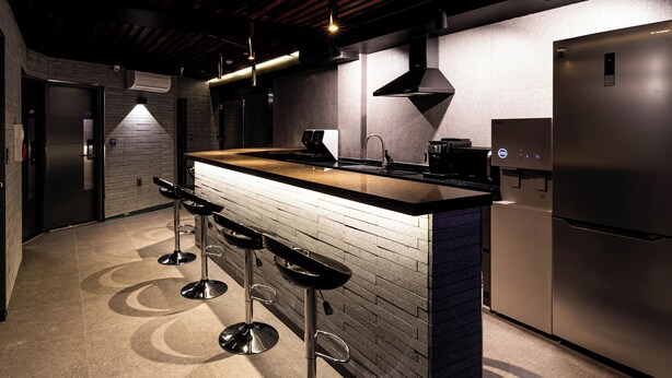 A modern kitchen with a central island, bar stools, stainless steel appliances, and a brick accent wall. - U STAY MyeongDong (Seoul)