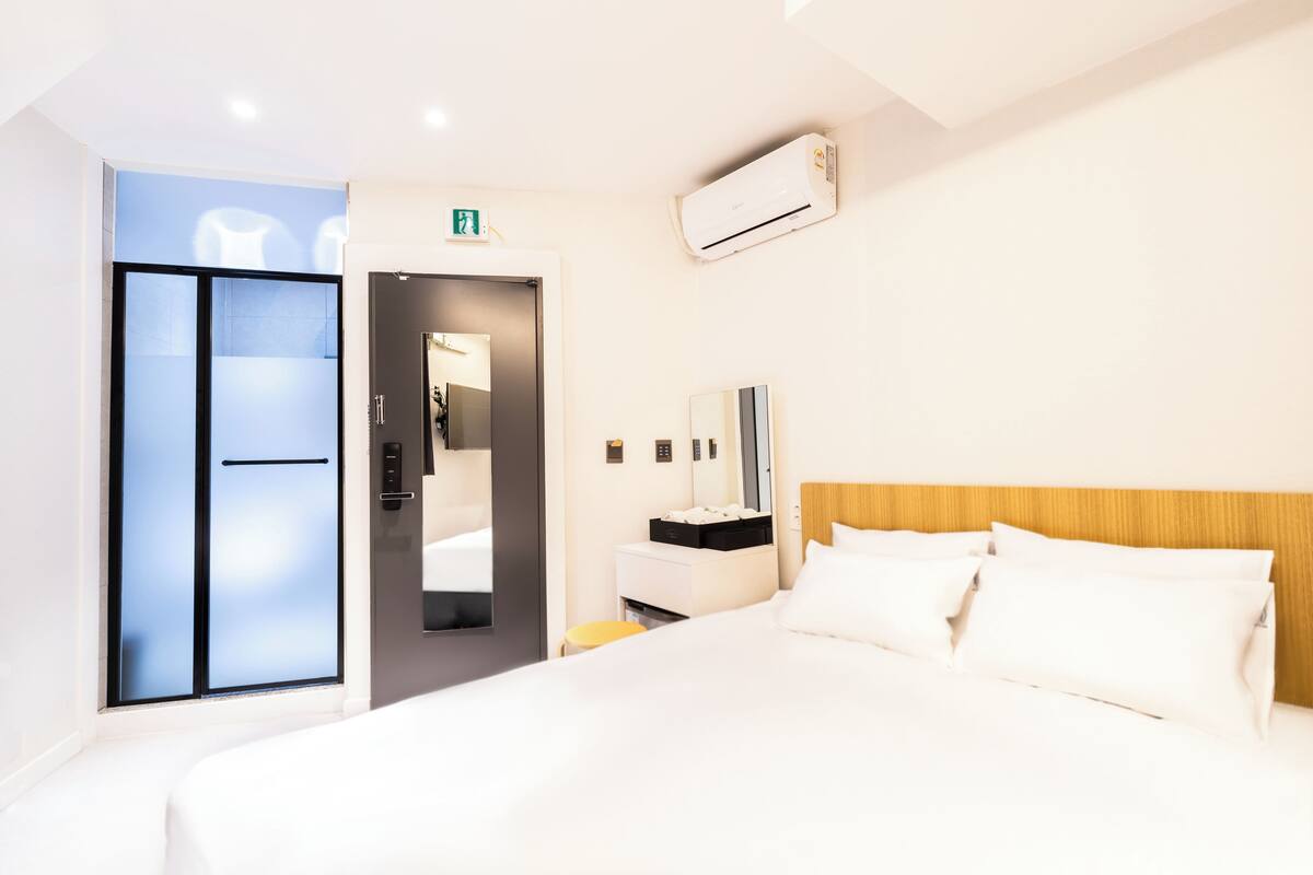 A modern hotel room with a large bed, a bedside table, a mirror, a wardrobe, and an air conditioning unit.