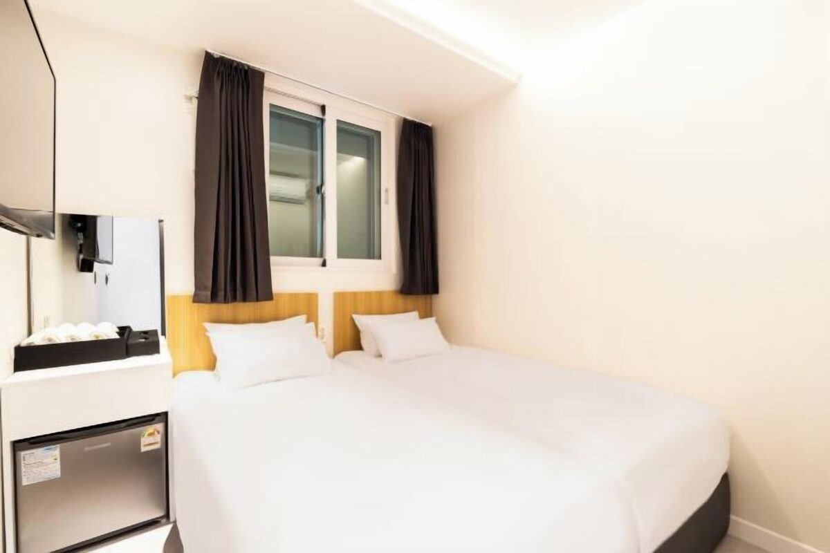 Habitación de hotel con cama, escritorio, espejo y ventana con cortinas.