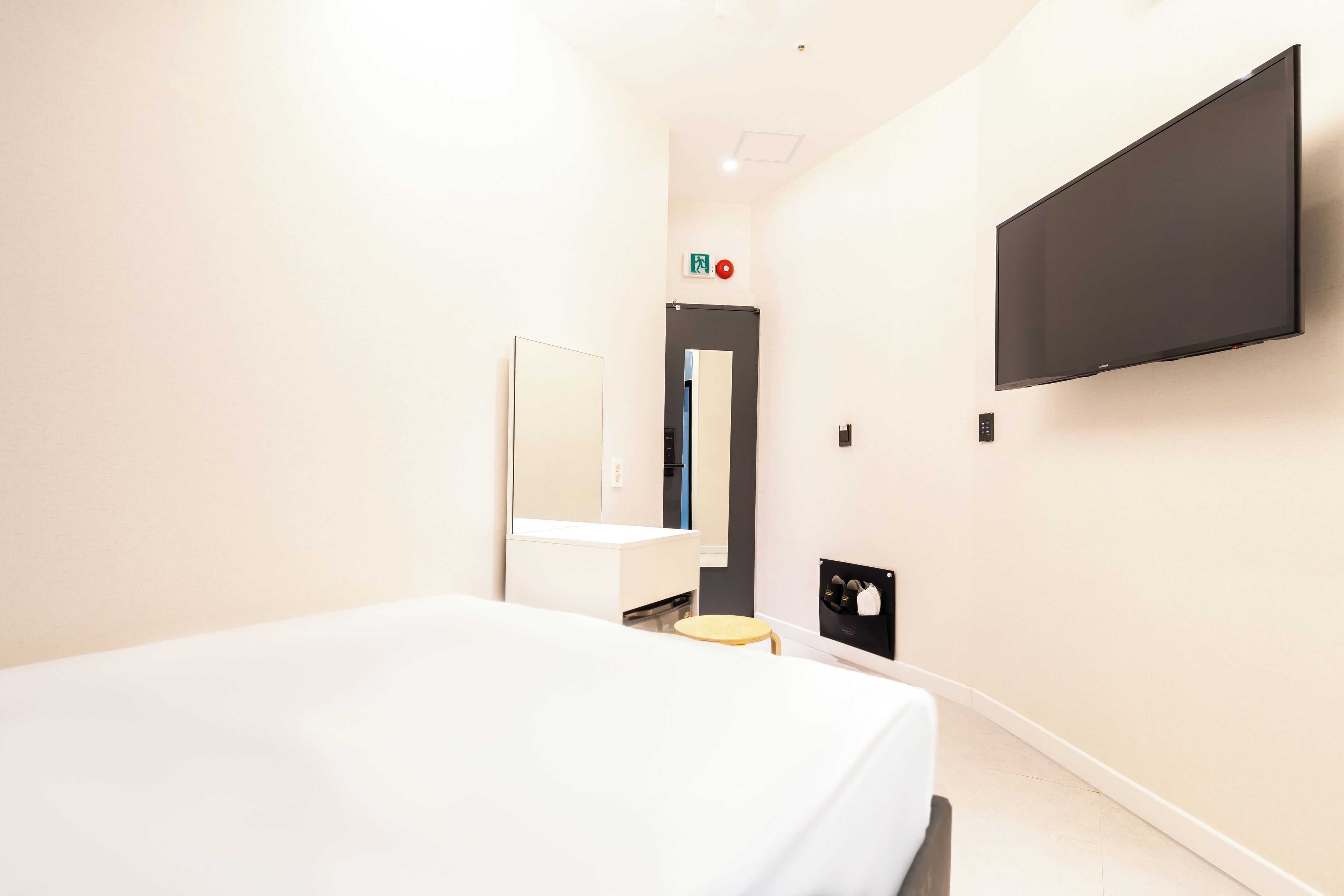 Una camera d'albergo con un letto, una TV a muro, uno sgabello e uno specchio.