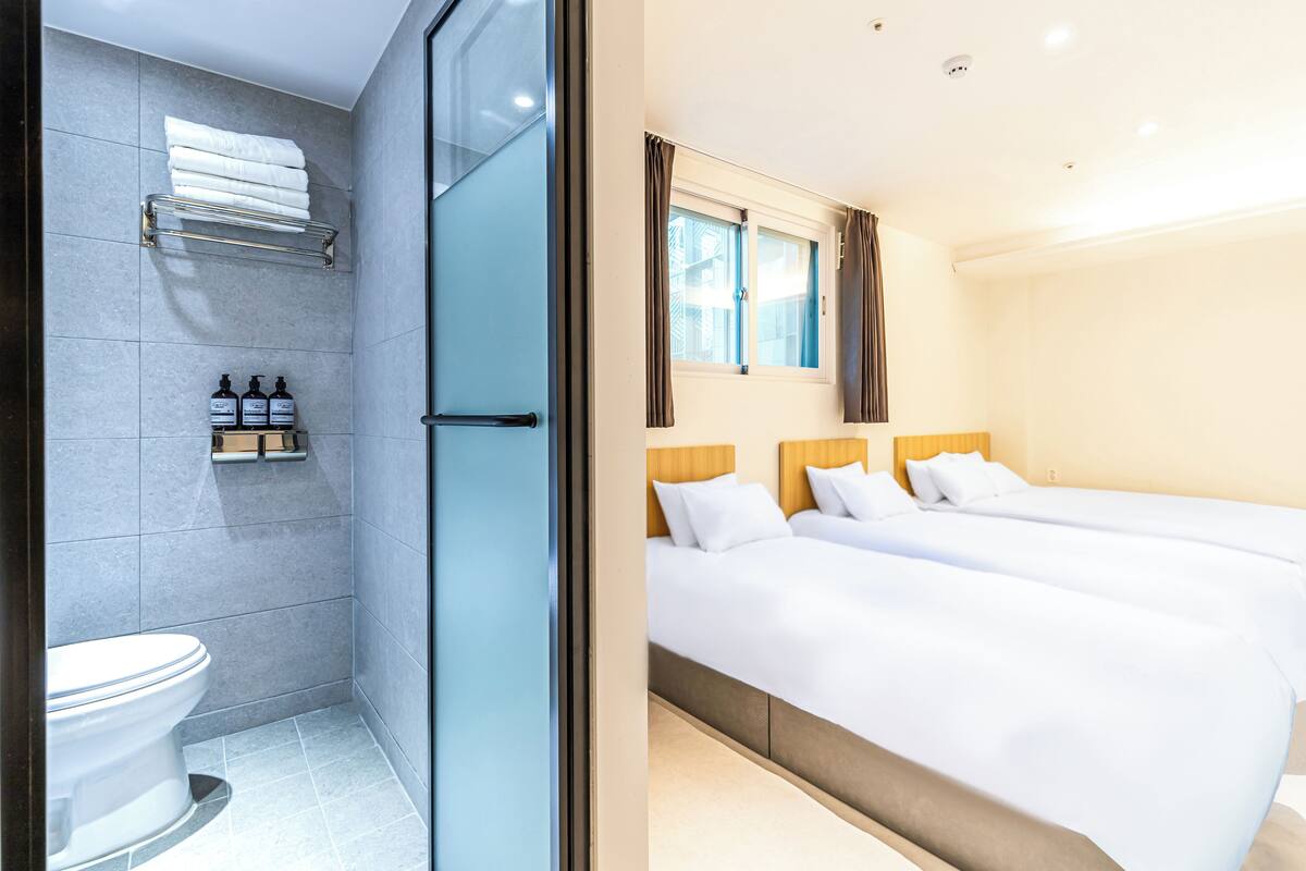 A modern hotel room with a shower, toilet, and two beds.