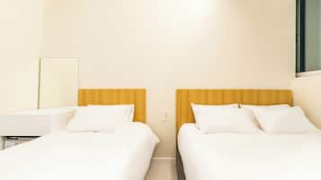 Hotellihuone, jossa on kaksi sänkyä, yöpöytä, peili ja ikkuna.