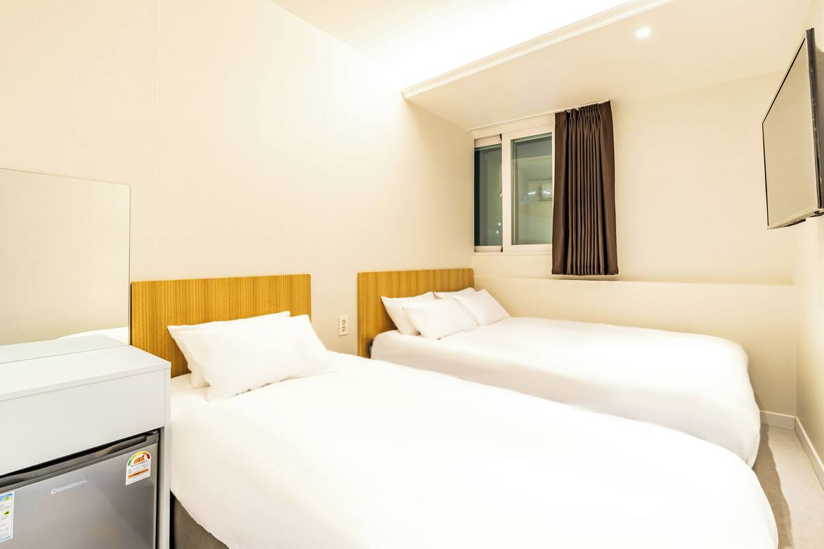 A hotel room with two beds, a minibar, a TV, and a window with curtains.