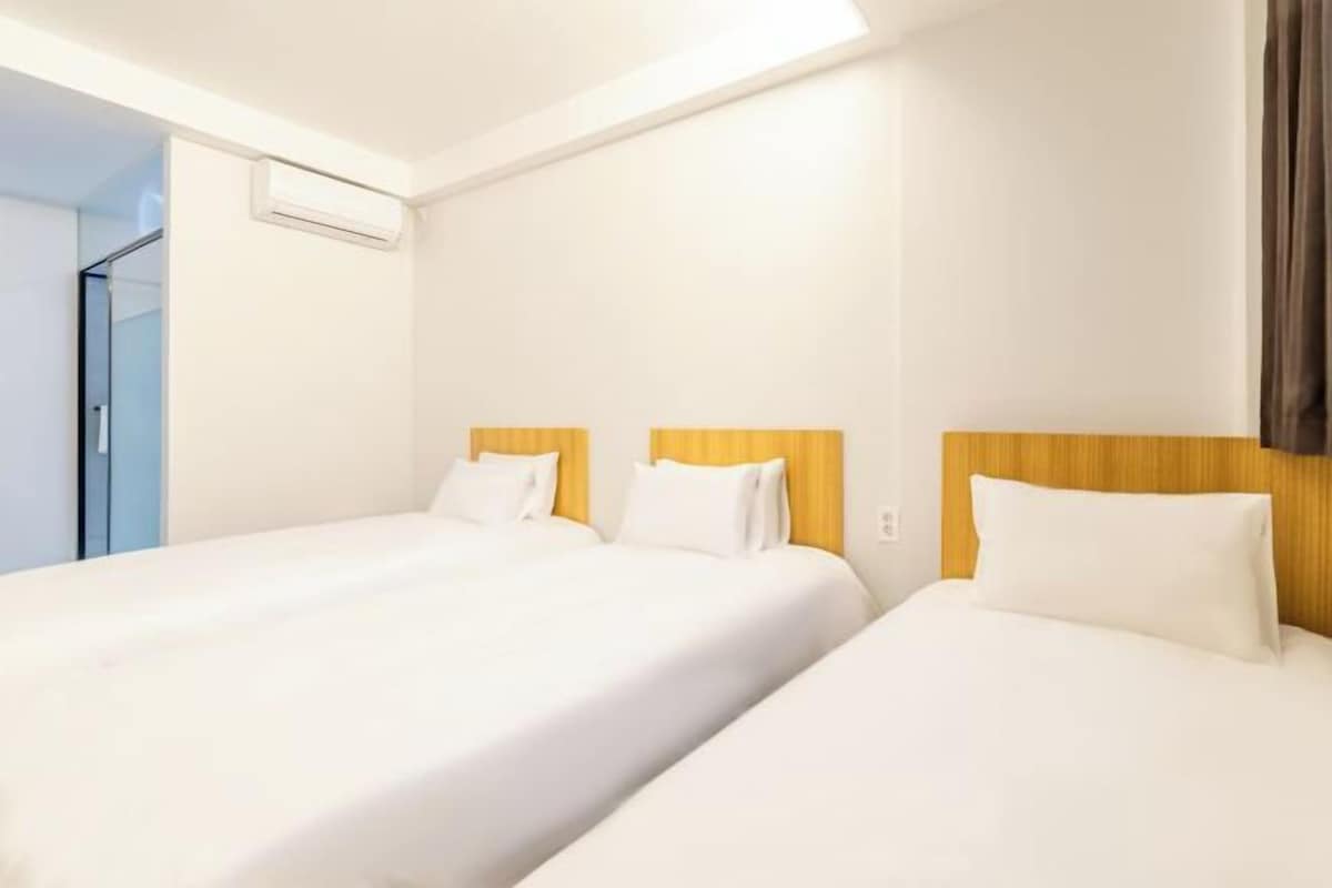 A hotel room with two beds, a wooden headboard, white bedding, and a visible air conditioning unit.