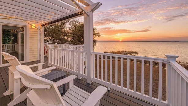 Un pontile in legno con ringhiere bianche e vista sul tramonto sull'acqua.