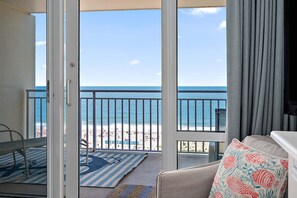 A room with a view of the beach, a balcony with a railing, and a patterned rug.