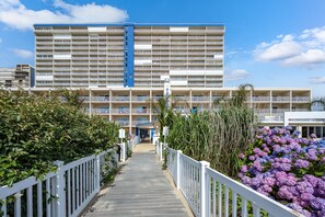 A multi-story hotel with a central entrance, a blue vertical accent, and a white fence surrounding the property.