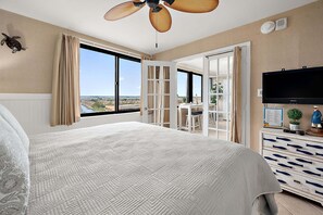 A hotel room with a large bed, a ceiling fan, a TV, and a view of the city.