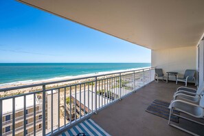 Un balcon avec vue sur la plage, une table, des chaises et un tapis à rayures.