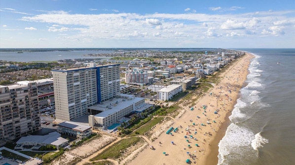 Paisagem costeira urbana com um hotel à beira-mar, com vários andares, piscina e acesso direto à praia.