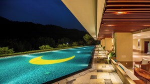 Ein Schwimmbecken mit einem gelben Halbmond-Design, einem überdachten Gang und Blick auf einen Berg in der Abenddämmerung.