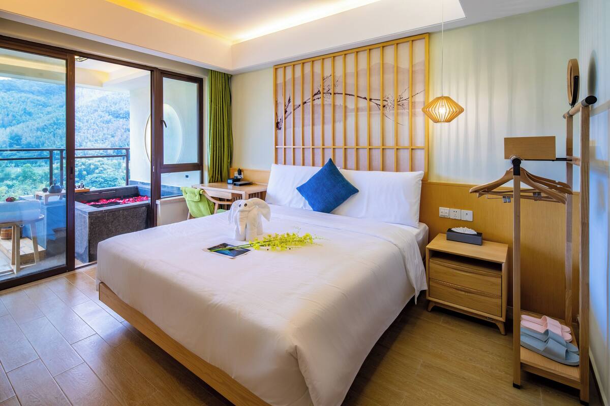 Ein Hotelzimmer mit einem großen Bett, einem hölzernen Kopfteil, einem Nachttisch, einer Lampe, einem Kleiderschrank und einem Balkon mit Bergblick.