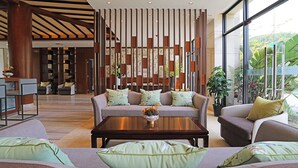 Eine großzügige Lobby mit modernem Design, ausgestattet mit einer zentralen Sitzecke mit Sofas und einem Couchtisch, umgeben von einer dekorativen Holzabtrennung.