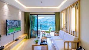 Ein modernes Wohnzimmer mit Fernseher, einer Couch, einem Couchtisch und Blick auf einen Balkon mit Bergblick.