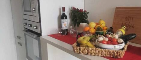 A kitchen with a microwave, oven, and a counter with a basket of fruits and vegetables.