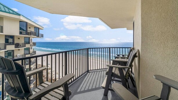A balcony with a view of the ocean, equipped with outdoor furniture and a covered area. - Fun N The Sun at Sunbird 1102W | Beach Chair Service Included | Oceanfront & Ocean View | 3 Pools (Panama City)