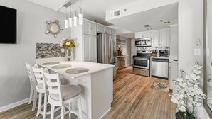 A modern kitchen with white cabinetry, a central island with bar stools, stainless steel appliances, and a backsplash with mosaic tiles. - Fun N The Sun at Sunbird 1102W | Beach Chair Service Included | Oceanfront & Ocean View | 3 Pools (Panama City)