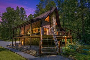 A log cabin with a stone chimney, wooden deck, and a staircase leading to the entrance.