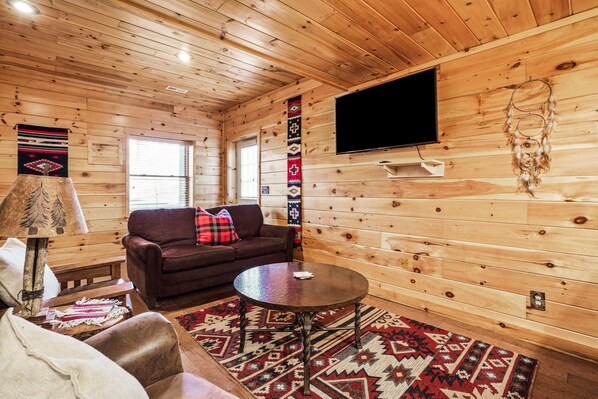 Ein gemütliches Blockhaus-Interieur mit Holzwänden, einer Couch, einem Couchtisch und einem an der Wand montierten Fernseher.