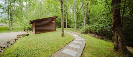 A wooden cabin with a gravel path leading to it, surrounded by a forested area.
