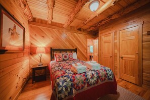 A cozy wooden cabin bedroom with a bed, a nightstand, a lamp, and a framed picture on the wall. - Arrowhead Lodge | Hocking Hills, Sauna & Hot Tub (Logan)