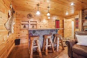 Ein Holzblockhaus-Interieur mit Barbereich, Barhocker, einem Ledersofa und einer Steinwand.