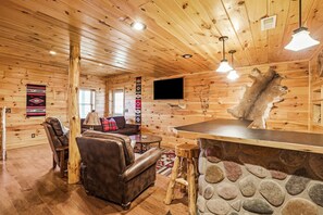 A log cabin interior with a stone fireplace, leather furniture, and a mounted television. - Arrowhead Lodge | Hocking Hills, Hot Tub, 5 Acres (Logan)