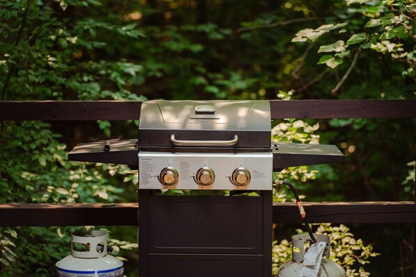 A portable gas grill with three control knobs, a digital display, and a gas tank.