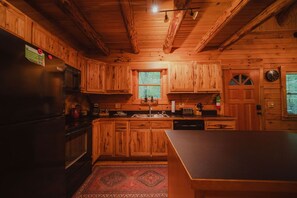 A wooden cabin interior with a kitchen area, including cabinets, a refrigerator, and a sink.