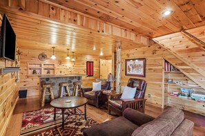 A cozy wooden cabin interior with a bar area, leather furniture, and a staircase.