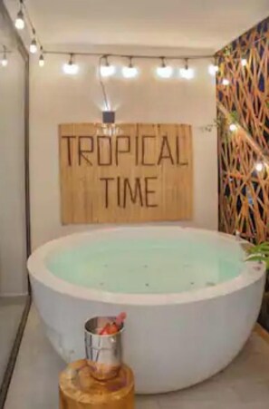 A spa area with a large circular hot tub, a wooden sign reading "TROPICAL TIME", and a decorative wall with hanging lights.