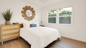 Une chambre à coucher avec un lit, une commode en bois, un miroir et une fenêtre donnant sur un paysage verdoyant.