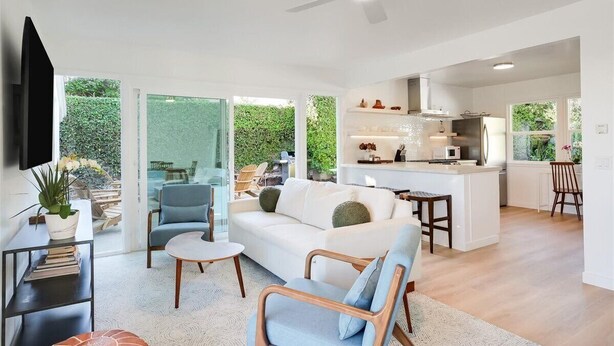 Un salon moderne avec un canapé, des fauteuils et une petite table. Il y a également un coin cuisine avec un comptoir et des appareils électroménagers.