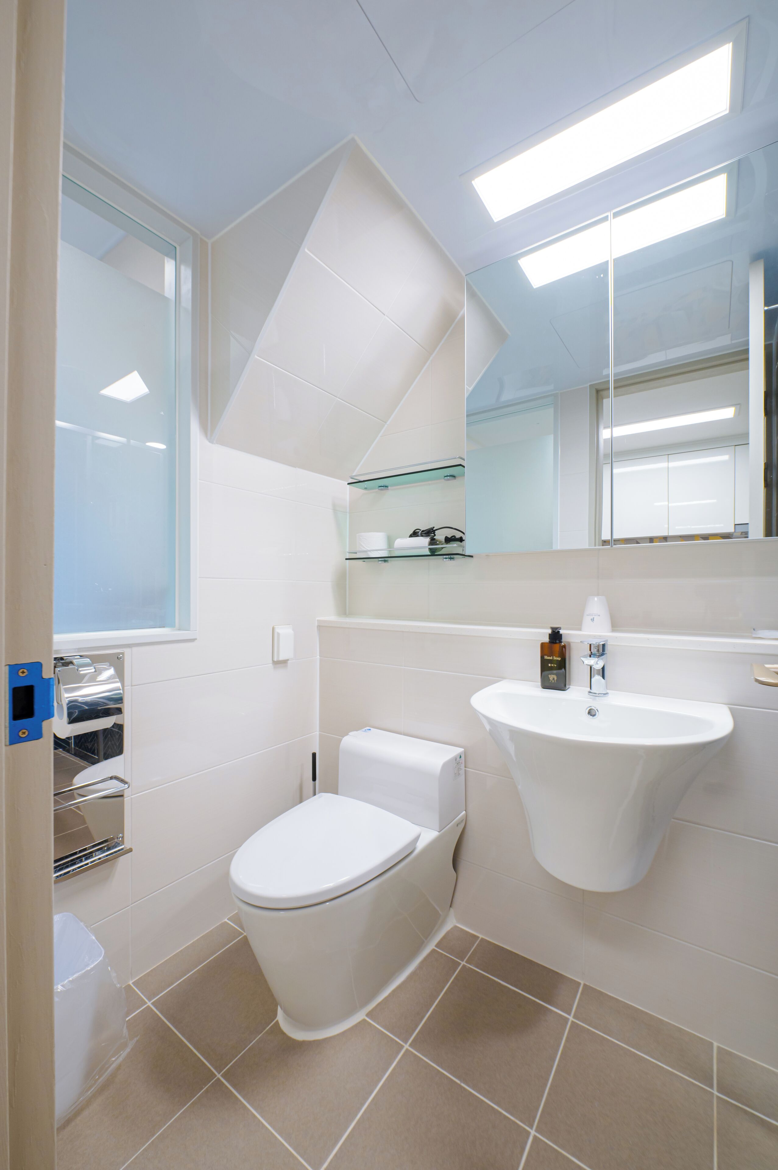 A modern bathroom with a toilet, sink, and glass shelving unit.