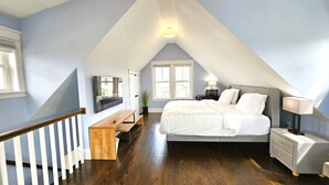 Una camera da letto con soffitto spiovente, un letto, un comodino, una lampada, una panca e una TV montata a parete.